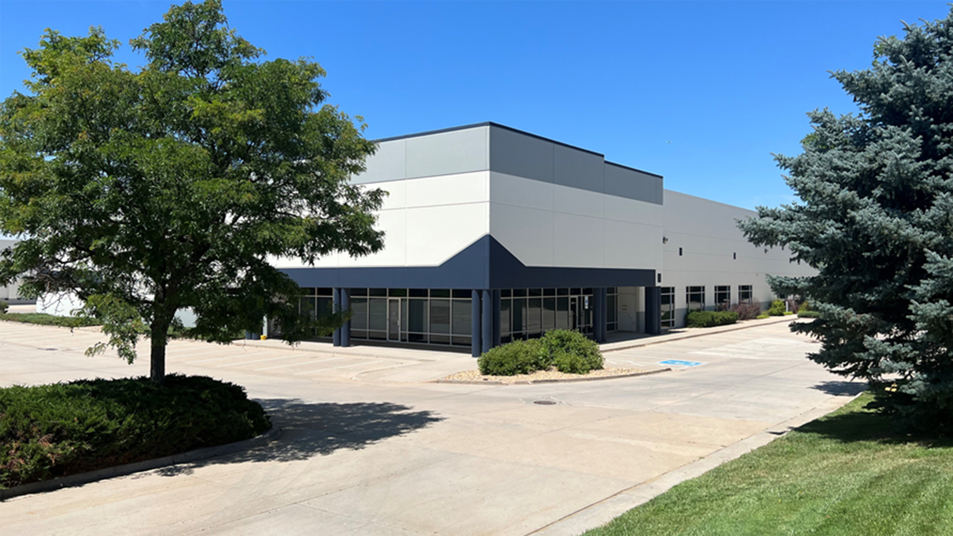 Exterior view of a modern industrial building with office and production areas, surrounded by trees and parking areas.